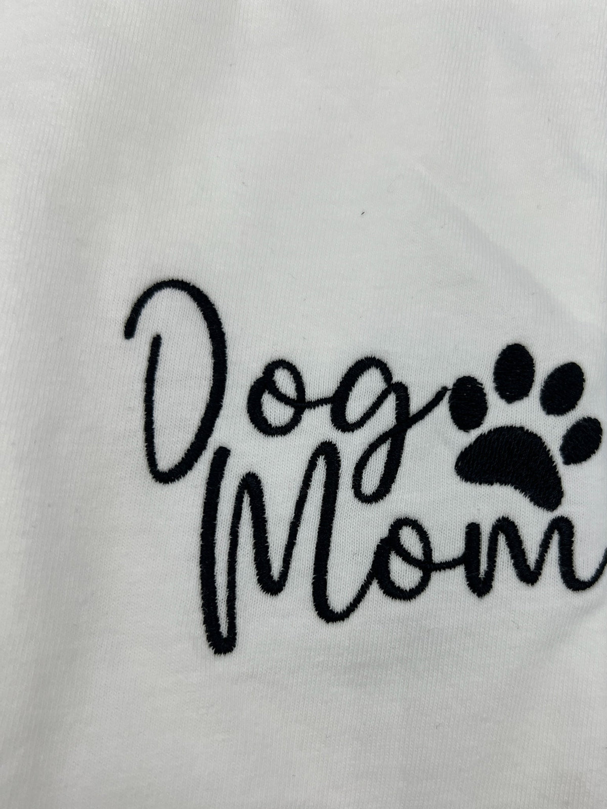 Nannette's Online Designs white cotton t-shirt featuring black embroidered Dog Mom text and a paw print design.