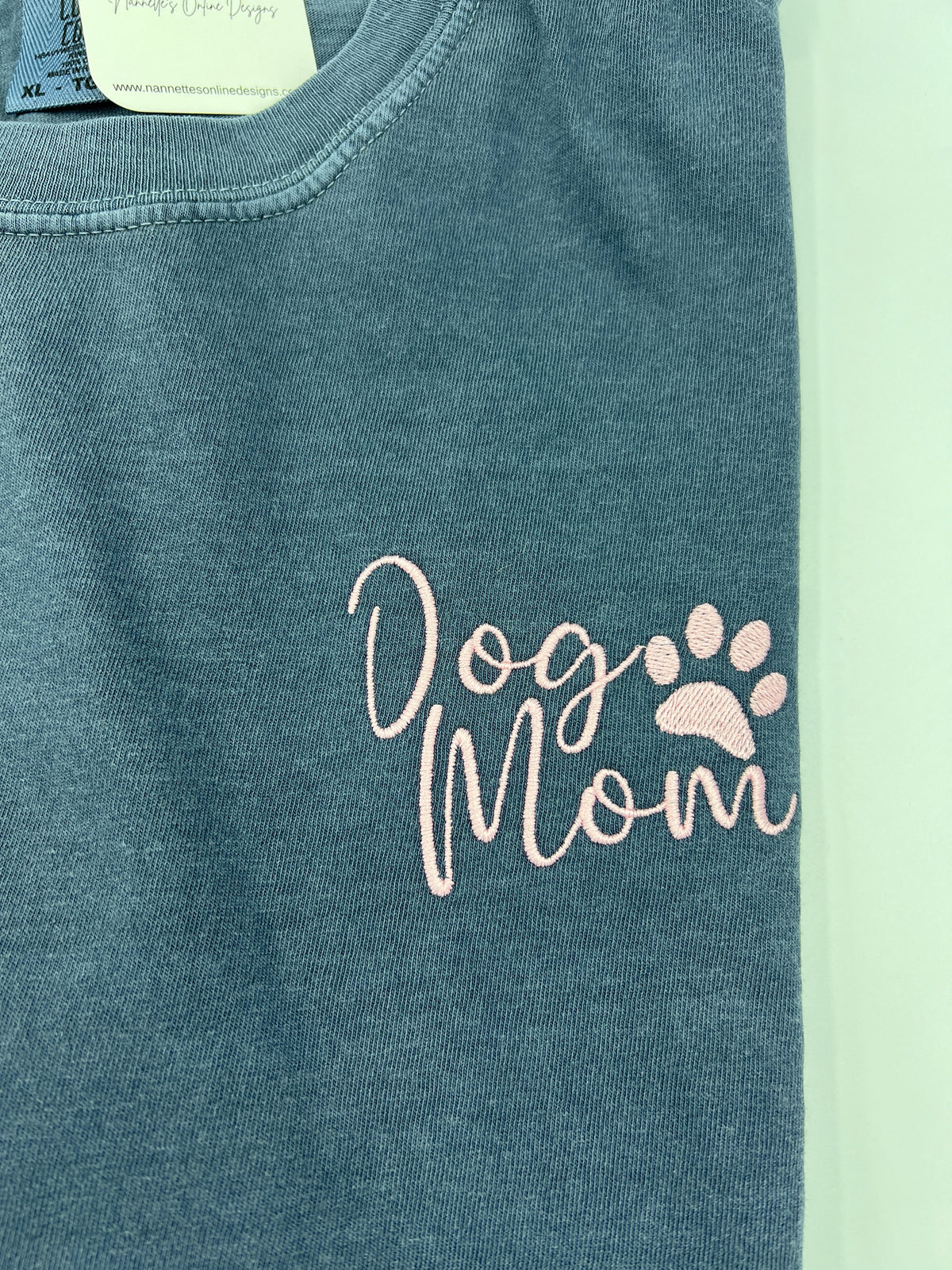 Nannette's Online Designs blue-grey garment-dyed cotton t-shirt with soft pink embroidered Dog Mom and paw print text.
