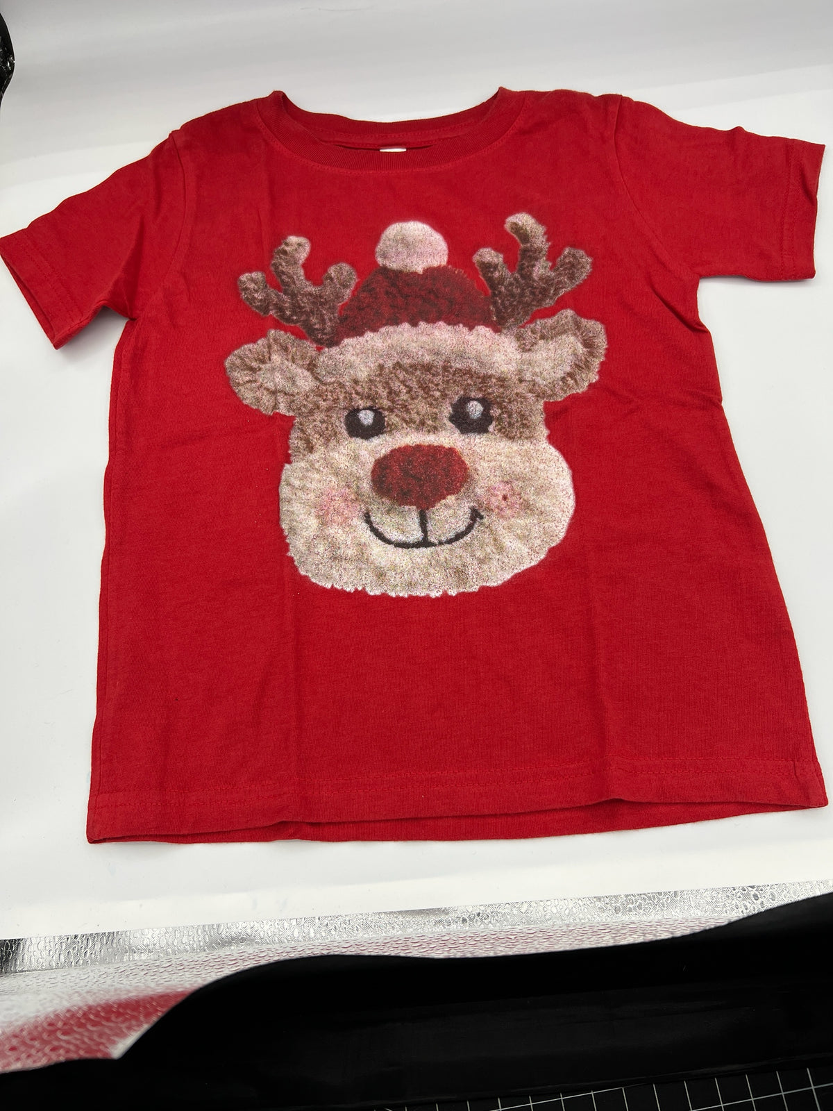 Nannette's Online Designs red short sleeve t-shirt featuring a textured reindeer graphic with a festive Santa hat