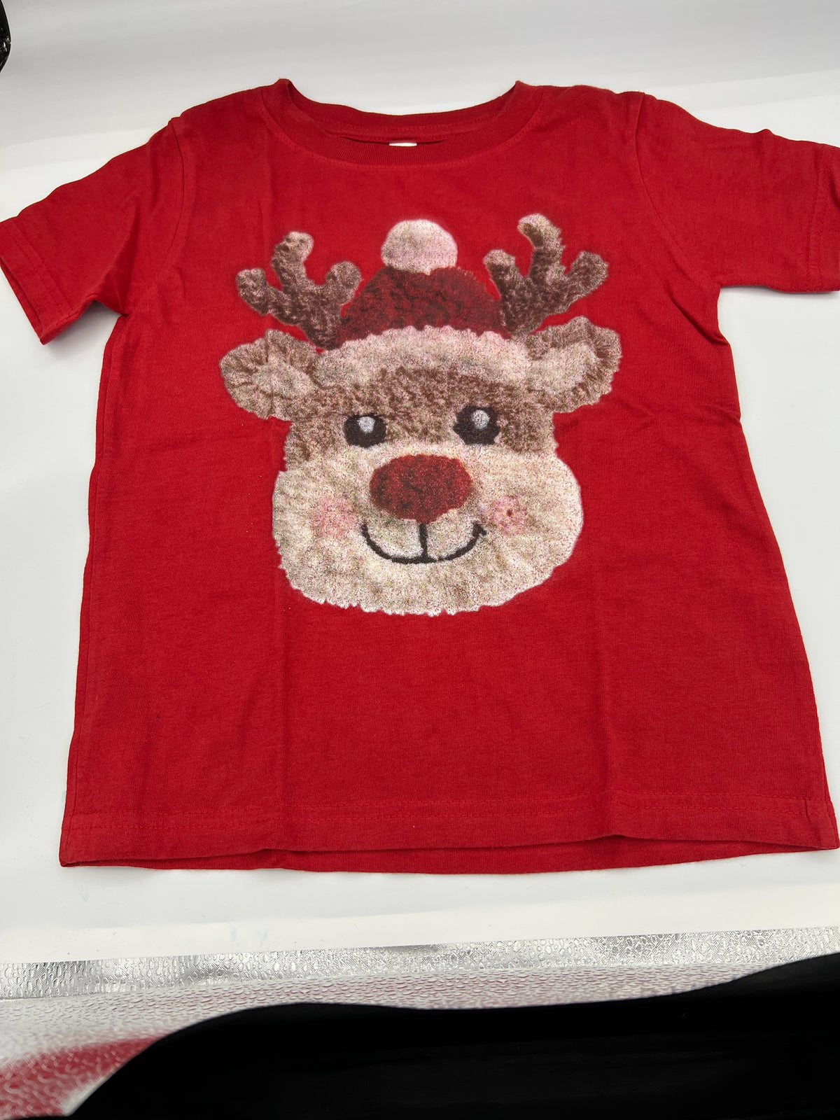 Nannette's Online Designs red short sleeve t-shirt featuring a textured reindeer graphic with a festive Santa hat.